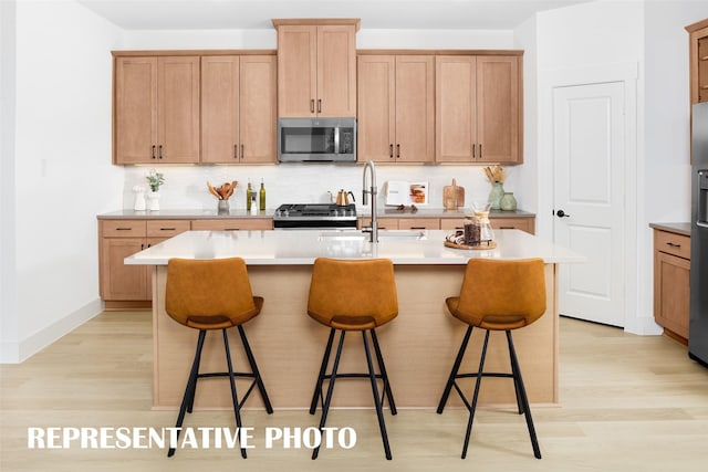 kitchen featuring a kitchen bar, appliances with stainless steel finishes, light wood-type flooring, and an island with sink