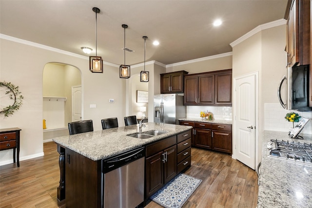 kitchen with sink, hanging light fixtures, appliances with stainless steel finishes, a kitchen breakfast bar, and a kitchen island with sink