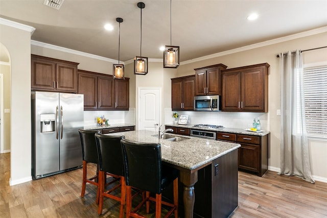 kitchen with sink, a kitchen island with sink, light stone counters, light hardwood / wood-style floors, and stainless steel appliances