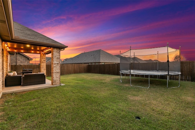 yard at dusk with a trampoline, an outdoor living space, and a patio area