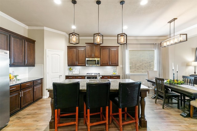 kitchen featuring appliances with stainless steel finishes, hanging light fixtures, light stone counters, light hardwood / wood-style floors, and a center island with sink