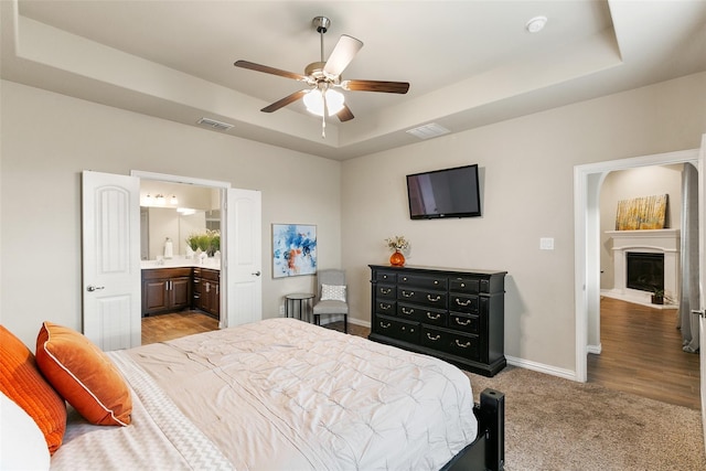 carpeted bedroom featuring ceiling fan, connected bathroom, and a tray ceiling