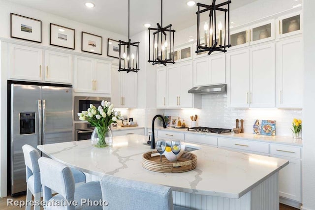 kitchen featuring stainless steel appliances, white cabinetry, hanging light fixtures, and an island with sink