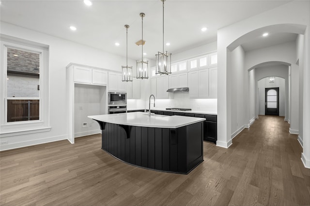 kitchen featuring arched walkways, a sink, under cabinet range hood, appliances with stainless steel finishes, and white cabinetry