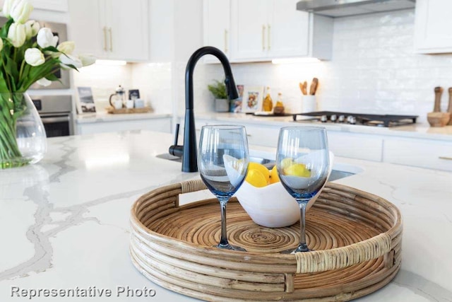 details featuring backsplash, light stone countertops, white cabinets, and extractor fan