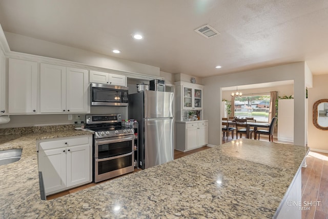 kitchen with light hardwood / wood-style floors, white cabinetry, stainless steel appliances, and a chandelier