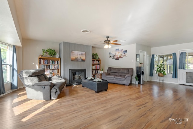 living room featuring ceiling fan, a large fireplace, a wealth of natural light, and light hardwood / wood-style flooring