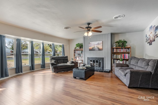 living room featuring ceiling fan, a large fireplace, light wood-type flooring, and a textured ceiling