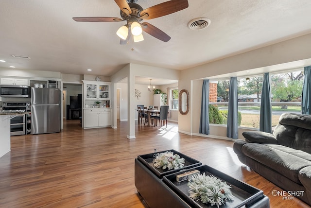 living room featuring wood-type flooring, ceiling fan with notable chandelier, and a textured ceiling