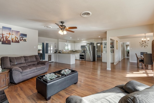 living room with ceiling fan with notable chandelier and light hardwood / wood-style floors