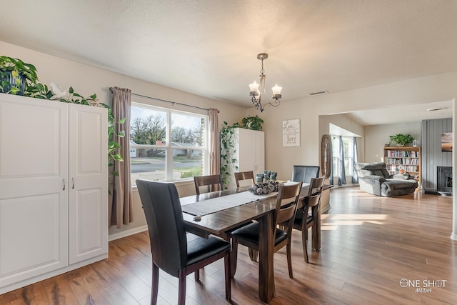 dining room featuring a notable chandelier, a fireplace, light wood-type flooring, and a textured ceiling