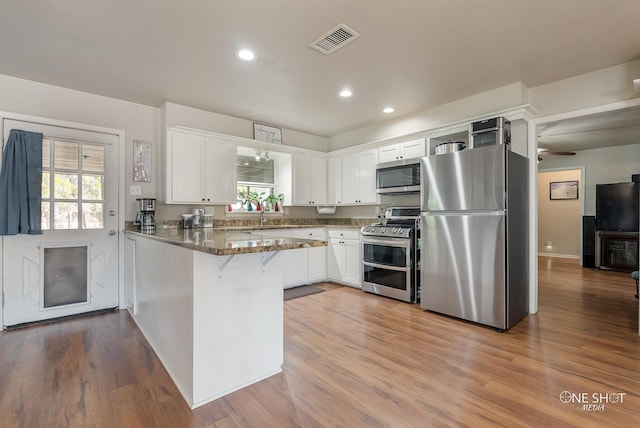 kitchen with kitchen peninsula, stainless steel appliances, dark stone countertops, white cabinets, and plenty of natural light