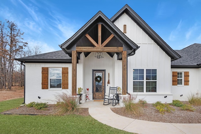 view of front of property with covered porch, roof with shingles, board and batten siding, and brick siding