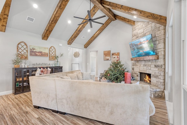 living room featuring a stone fireplace, beamed ceiling, high vaulted ceiling, and light hardwood / wood-style floors