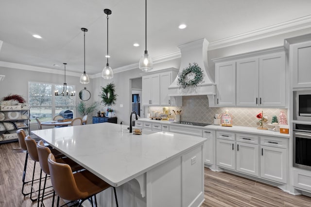 kitchen featuring stainless steel oven, premium range hood, sink, an island with sink, and stovetop