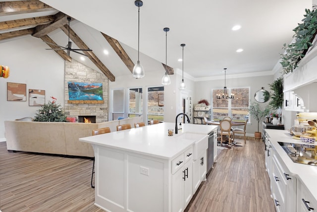 kitchen featuring white cabinets, a center island with sink, a stone fireplace, and hanging light fixtures