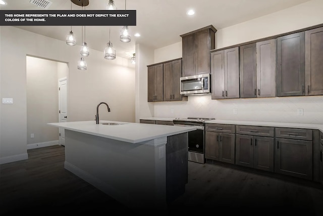 kitchen with dark wood-type flooring, sink, an island with sink, decorative light fixtures, and stainless steel appliances