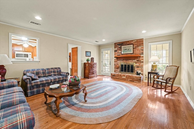 living room featuring light hardwood / wood-style flooring, a brick fireplace, ceiling fan, and crown molding