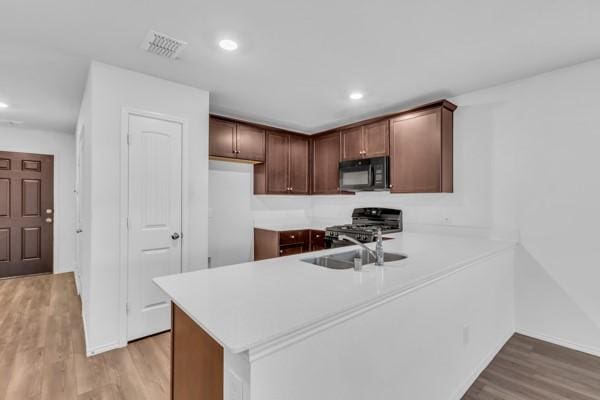 kitchen featuring kitchen peninsula, light hardwood / wood-style flooring, black appliances, and sink