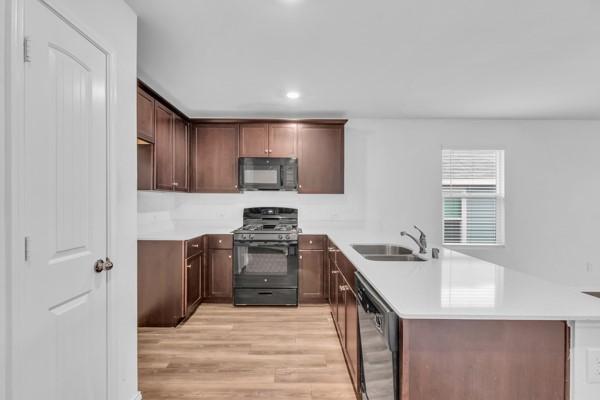 kitchen with black appliances, sink, light hardwood / wood-style flooring, dark brown cabinets, and kitchen peninsula