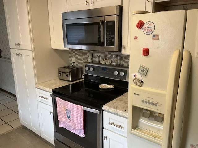 kitchen with backsplash, light stone countertops, light tile patterned floors, white cabinetry, and stainless steel appliances