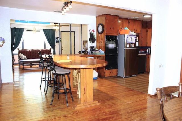 kitchen featuring stainless steel refrigerator, ceiling fan, black double oven, and wood-type flooring