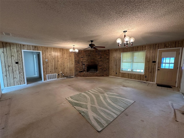 unfurnished living room featuring carpet flooring, a brick fireplace, ceiling fan with notable chandelier, a textured ceiling, and wooden walls