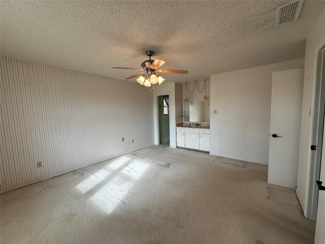 unfurnished living room with ceiling fan, sink, a textured ceiling, and light carpet