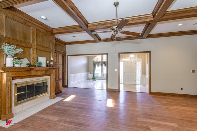 unfurnished living room with coffered ceiling, ceiling fan with notable chandelier, hardwood / wood-style flooring, beamed ceiling, and a tiled fireplace