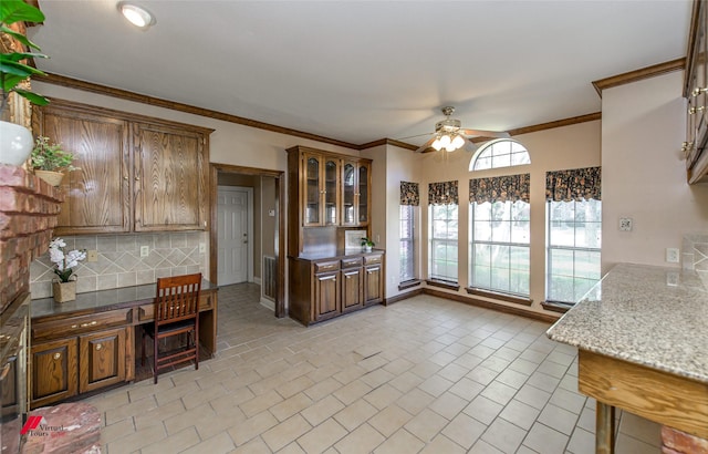 kitchen featuring built in desk, tasteful backsplash, ornamental molding, ceiling fan, and light stone countertops