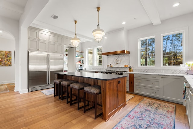 kitchen with built in refrigerator, beamed ceiling, custom range hood, and light wood-type flooring