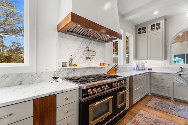 kitchen featuring light stone counters, light hardwood / wood-style flooring, range with two ovens, gray cabinets, and custom exhaust hood