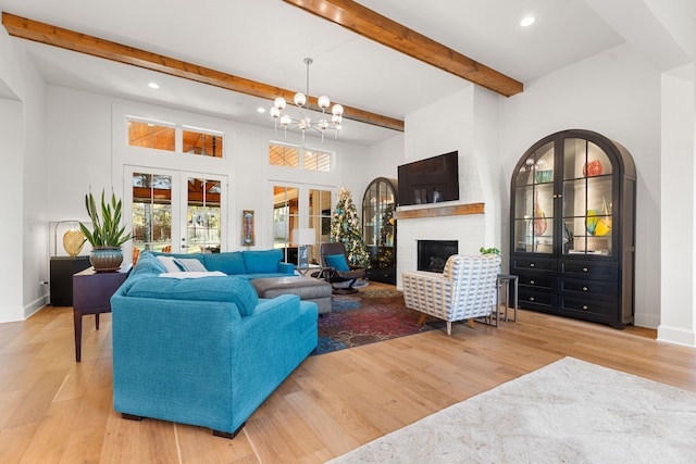 living room featuring french doors, a fireplace, beamed ceiling, light hardwood / wood-style floors, and a chandelier