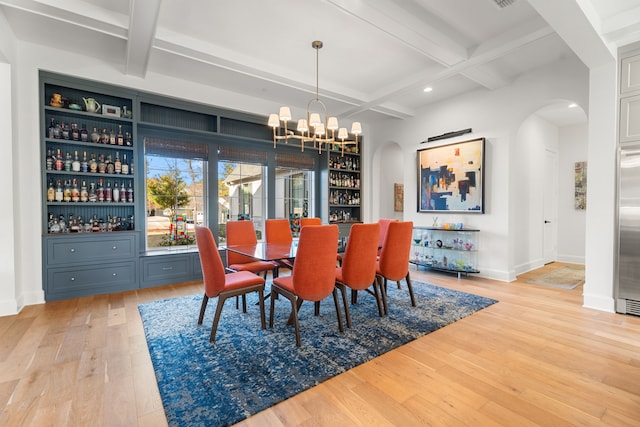 dining room with coffered ceiling, beamed ceiling, a notable chandelier, bar area, and light hardwood / wood-style floors