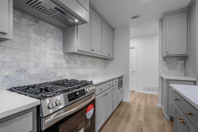 kitchen with light hardwood / wood-style flooring, gray cabinets, wall chimney exhaust hood, and appliances with stainless steel finishes