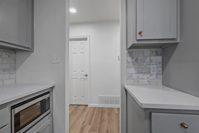 kitchen with stainless steel microwave, decorative backsplash, and gray cabinets