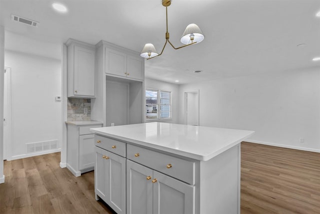 kitchen featuring gray cabinetry, a center island, decorative backsplash, decorative light fixtures, and light wood-type flooring