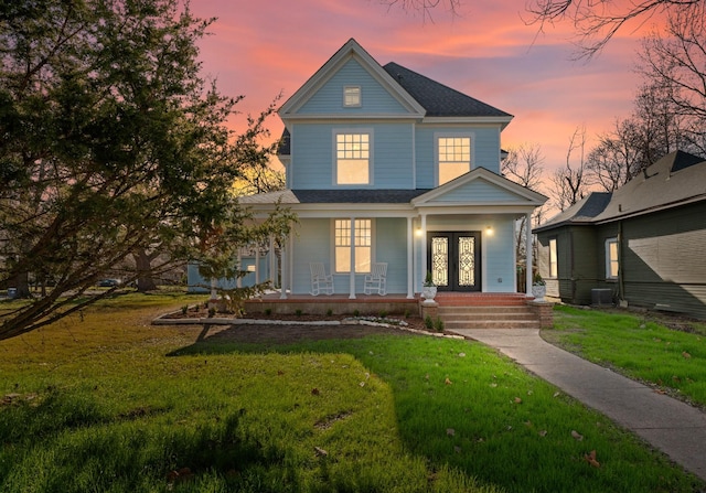 view of front of home featuring a lawn, covered porch, and french doors