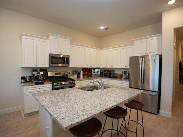 kitchen with stainless steel appliances, white cabinetry, sink, and a center island with sink