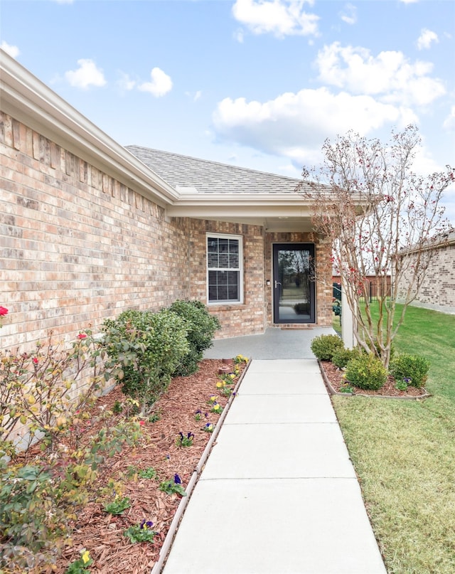 property entrance featuring brick siding, a lawn, and roof with shingles