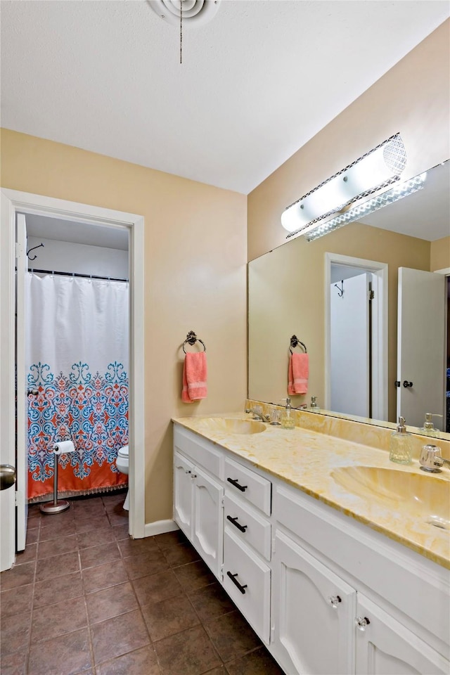 bathroom with double vanity, toilet, a sink, and tile patterned floors