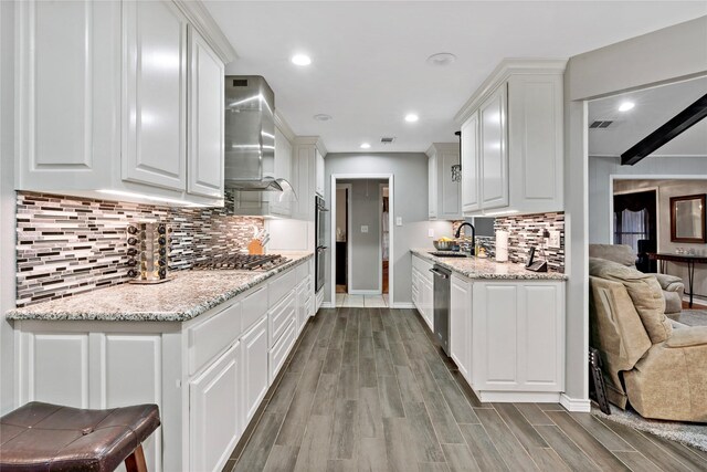 kitchen featuring white cabinetry, sink, wall chimney range hood, light hardwood / wood-style flooring, and appliances with stainless steel finishes