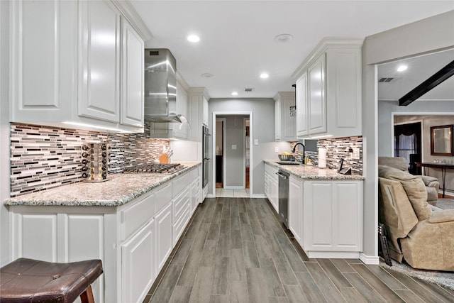 kitchen featuring stainless steel appliances, wall chimney range hood, a sink, and white cabinetry