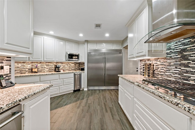 kitchen featuring wall chimney exhaust hood, dark hardwood / wood-style flooring, white cabinetry, and stainless steel appliances