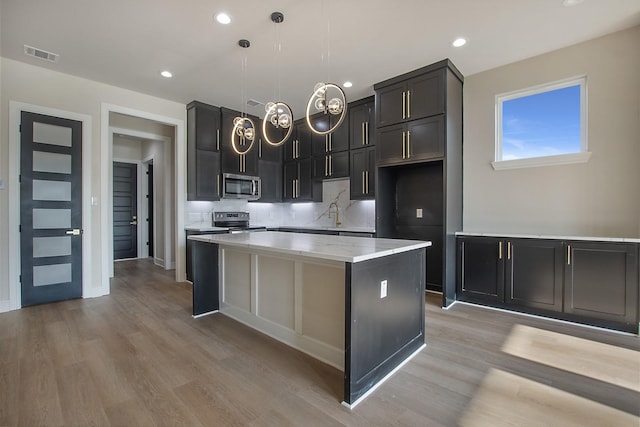 kitchen with light hardwood / wood-style flooring, appliances with stainless steel finishes, a center island, decorative backsplash, and decorative light fixtures