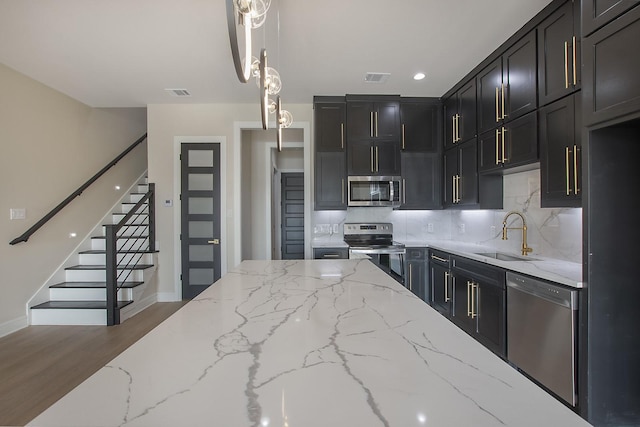 kitchen featuring light stone countertops, dark hardwood / wood-style floors, backsplash, pendant lighting, and appliances with stainless steel finishes