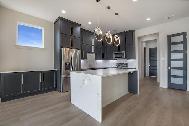 kitchen featuring tasteful backsplash, a center island, hanging light fixtures, light wood-type flooring, and stainless steel appliances