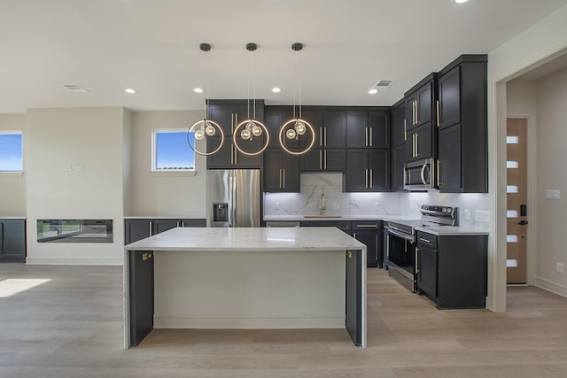 kitchen with a kitchen island, appliances with stainless steel finishes, pendant lighting, sink, and light stone countertops