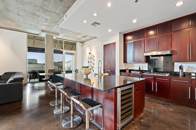 kitchen with a breakfast bar, a center island with sink, beverage cooler, and stainless steel gas stovetop