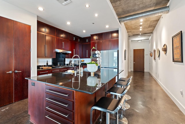 kitchen with stainless steel appliances, sink, dark stone countertops, a breakfast bar area, and an island with sink